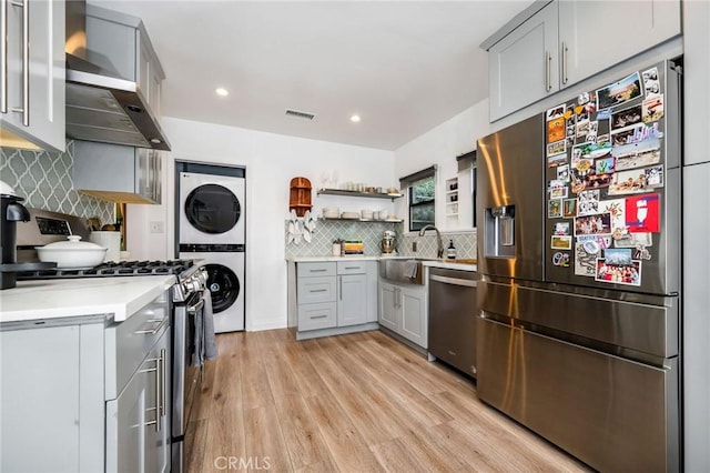 kitchen featuring wall chimney range hood, light countertops, gray cabinets, stacked washing maching and dryer, and stainless steel appliances