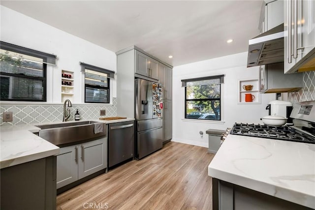 kitchen with gray cabinets, a sink, light stone counters, backsplash, and appliances with stainless steel finishes