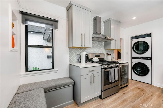 kitchen featuring stainless steel gas range oven, stacked washer and dryer, beverage cooler, gray cabinets, and wall chimney range hood