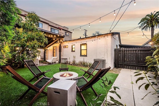 back of property featuring a fire pit, fence, central AC, stucco siding, and a yard