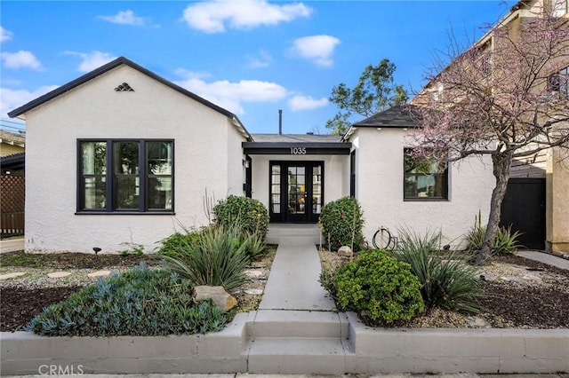 view of front facade with stucco siding, french doors, and fence