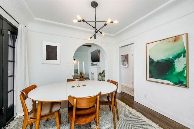 dining room featuring arched walkways, a notable chandelier, baseboards, and dark wood-style flooring