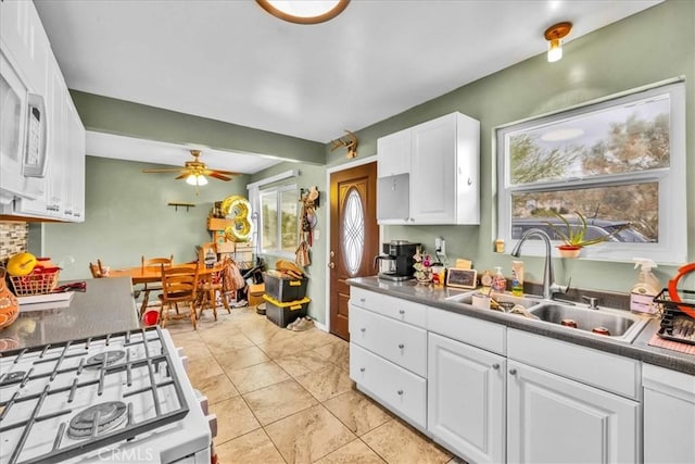 kitchen with white cabinets, white gas stove, ceiling fan, and a sink