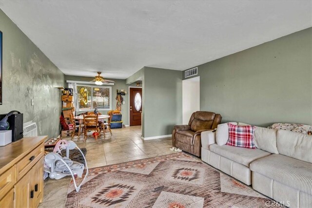 living room featuring light tile patterned floors, visible vents, baseboards, and a ceiling fan