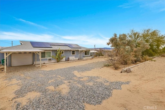 ranch-style home with solar panels, gravel driveway, a garage, and stucco siding