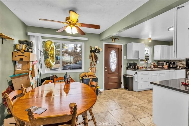 kitchen featuring dark countertops, a ceiling fan, a sink, light tile patterned floors, and white cabinets