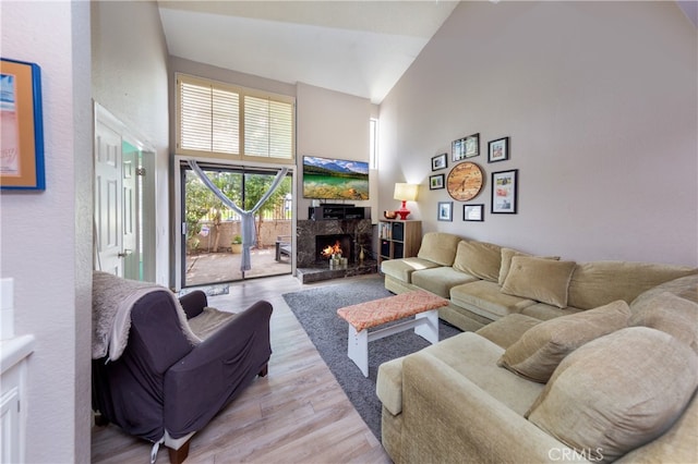 living room featuring wood finished floors, a warm lit fireplace, and high vaulted ceiling