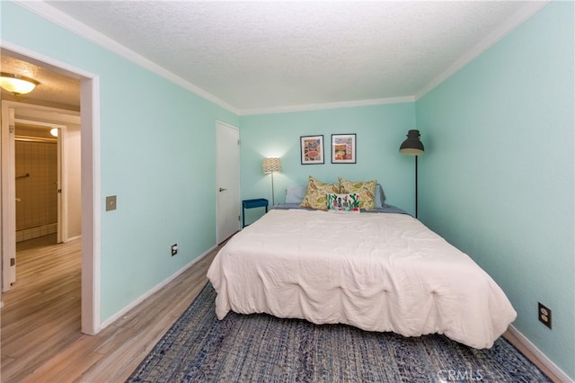 bedroom featuring baseboards, a textured ceiling, wood finished floors, and crown molding