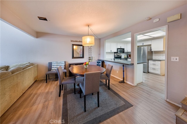 dining area featuring light wood-style flooring, baseboards, visible vents, and a textured ceiling