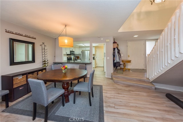 dining room featuring stairway, baseboards, and light wood-type flooring