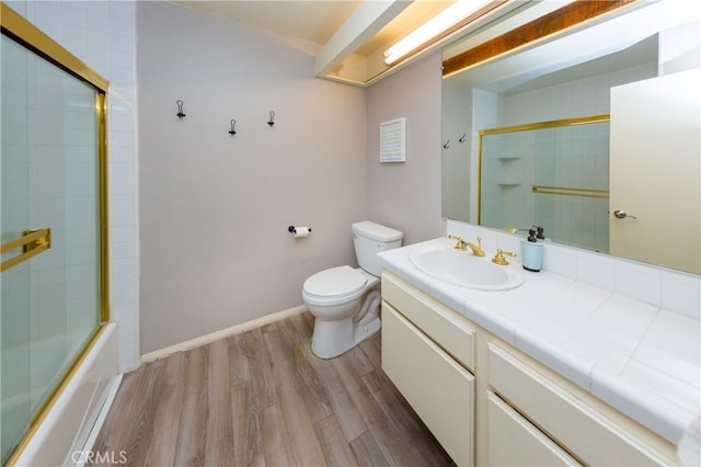 bathroom with baseboards, toilet, wood finished floors, combined bath / shower with glass door, and vanity