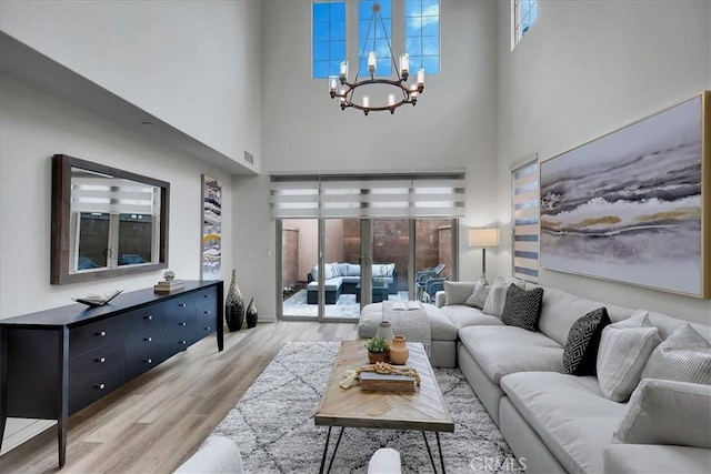 living area with an inviting chandelier, a high ceiling, visible vents, and light wood-type flooring