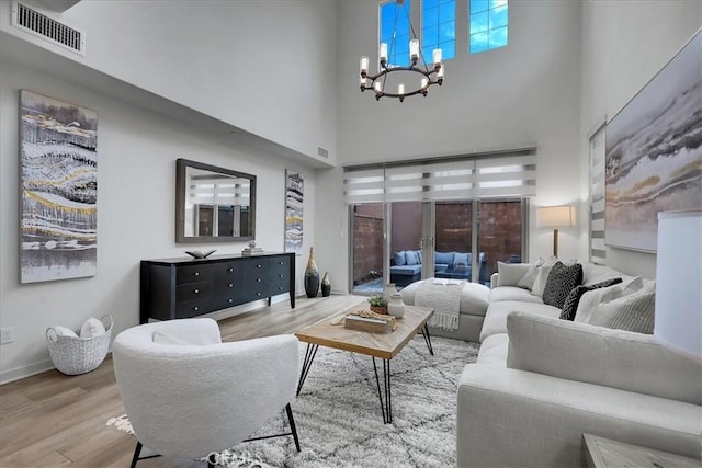 living room featuring visible vents, a notable chandelier, wood finished floors, a high ceiling, and baseboards