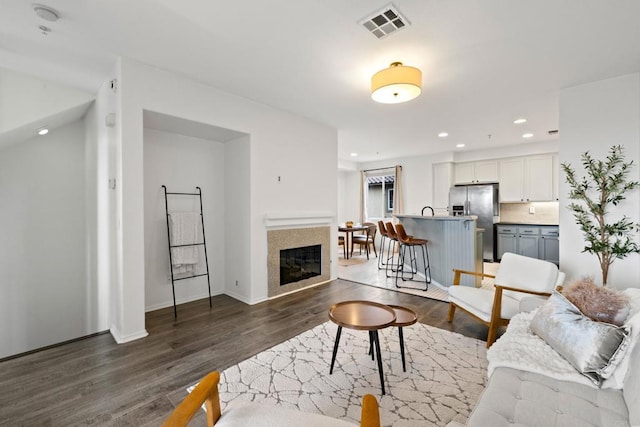 living area with visible vents, recessed lighting, dark wood-type flooring, and a glass covered fireplace