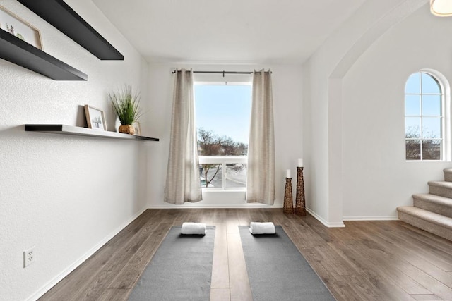 exercise area with wood finished floors, baseboards, and arched walkways