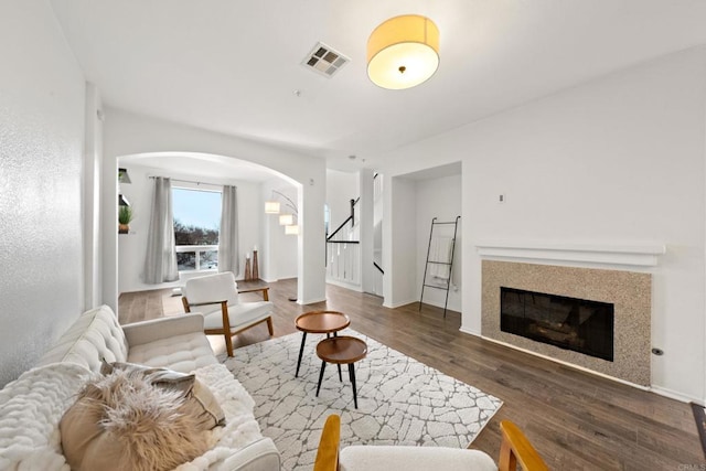 living area with visible vents, a glass covered fireplace, wood finished floors, arched walkways, and stairs