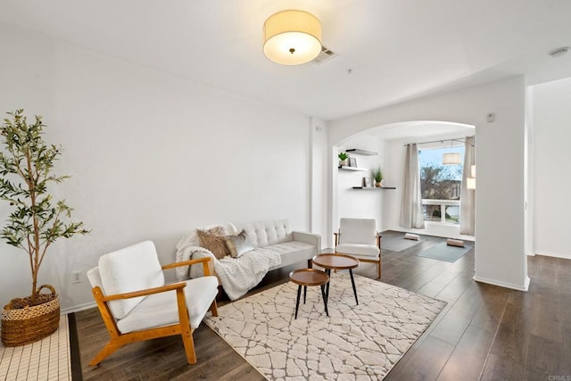 living room with arched walkways, dark wood-style floors, baseboards, and visible vents