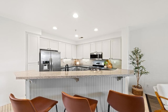 kitchen with stainless steel appliances, a kitchen bar, backsplash, and white cabinets