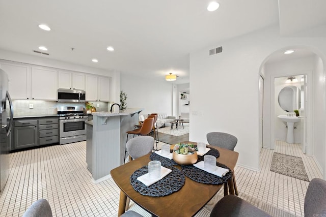 kitchen with visible vents, a kitchen bar, gray cabinets, arched walkways, and stainless steel appliances