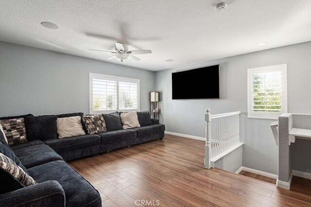 living room featuring ceiling fan, a textured ceiling, baseboards, and wood finished floors