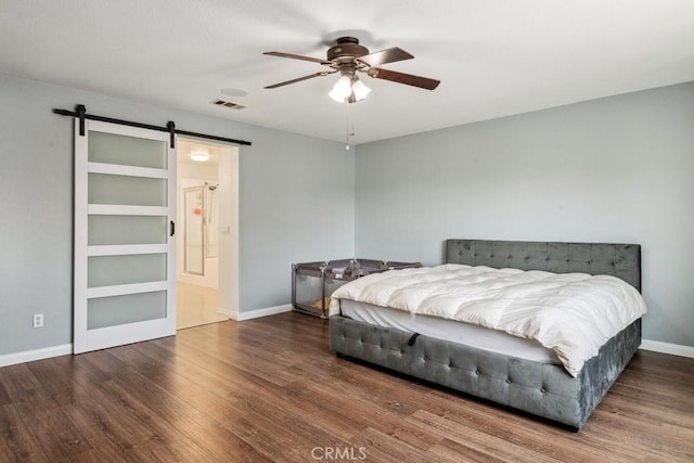 bedroom with visible vents, wood finished floors, a barn door, baseboards, and ceiling fan