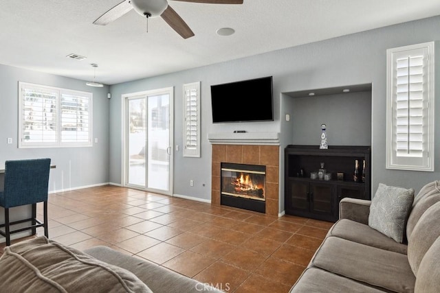 tiled living area featuring visible vents, baseboards, a ceiling fan, and a tile fireplace