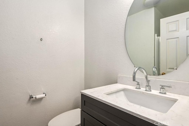 bathroom featuring toilet, vanity, and a textured wall