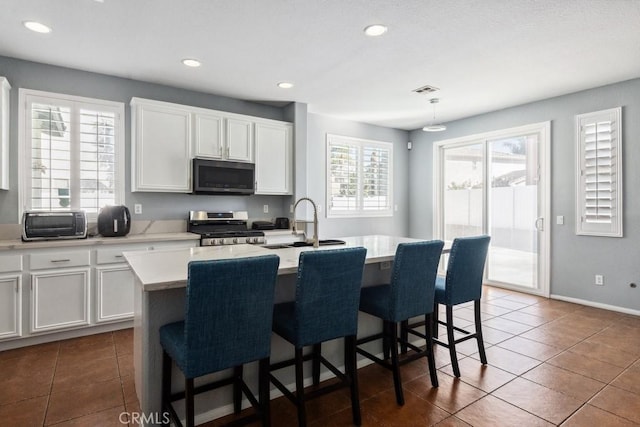 kitchen with an island with sink, light countertops, appliances with stainless steel finishes, white cabinetry, and a kitchen breakfast bar