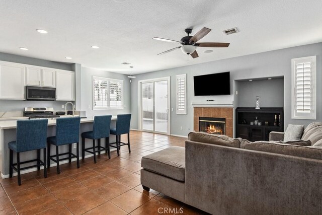 living room with a ceiling fan, visible vents, dark tile patterned flooring, a tile fireplace, and a textured ceiling