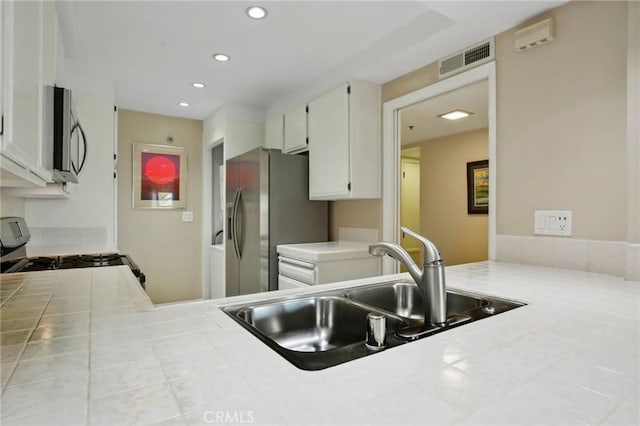 kitchen with tile counters, visible vents, appliances with stainless steel finishes, and a sink