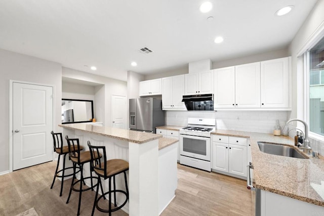 kitchen with a sink, stainless steel fridge, light wood-style flooring, and white gas range oven