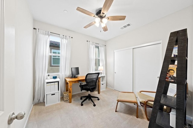 office area with baseboards, a ceiling fan, visible vents, and light carpet