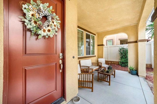 entrance to property featuring stucco siding, a porch, and fence