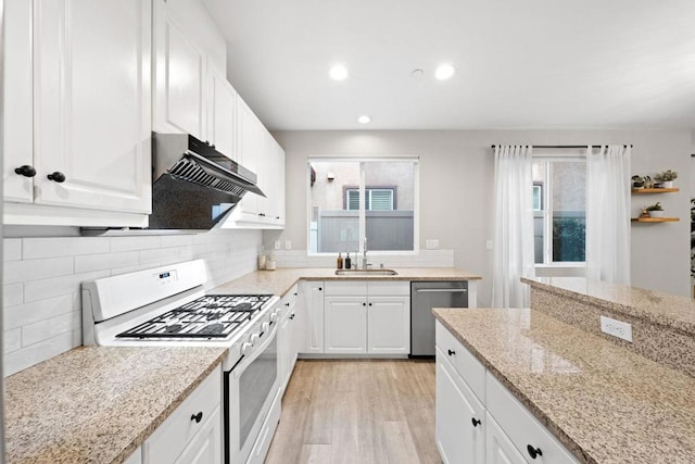 kitchen featuring white gas stove, a sink, white cabinets, under cabinet range hood, and stainless steel dishwasher