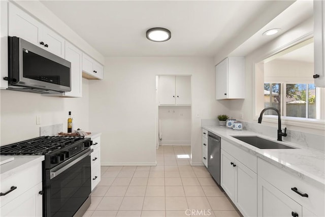 kitchen with a sink, stainless steel appliances, white cabinets, light tile patterned floors, and baseboards