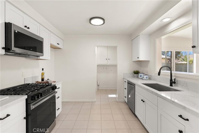 kitchen with white cabinetry, appliances with stainless steel finishes, light tile patterned flooring, a sink, and baseboards