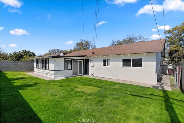 rear view of house featuring a gate, a yard, fence, and stucco siding