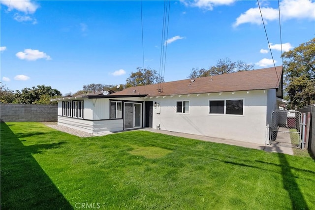 back of property featuring a yard, stucco siding, fence, and a gate