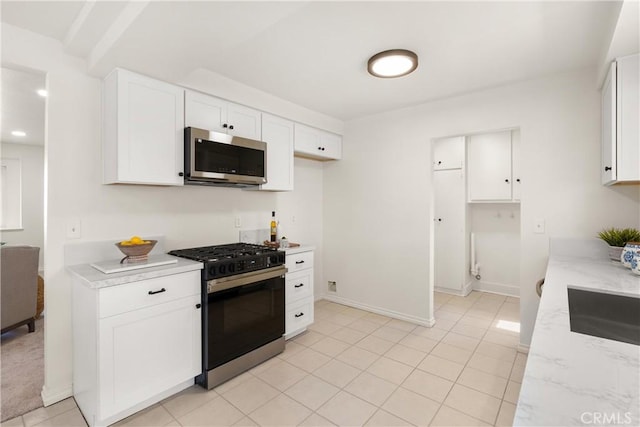 kitchen with a sink, stainless steel microwave, range with gas stovetop, white cabinets, and light stone countertops