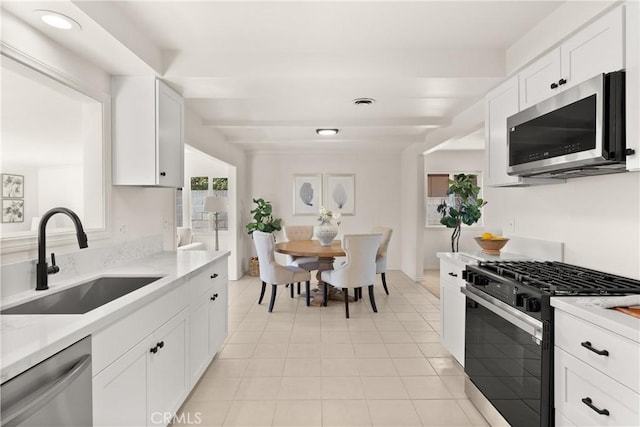 kitchen with light tile patterned floors, white cabinets, a sink, light countertops, and stainless steel appliances