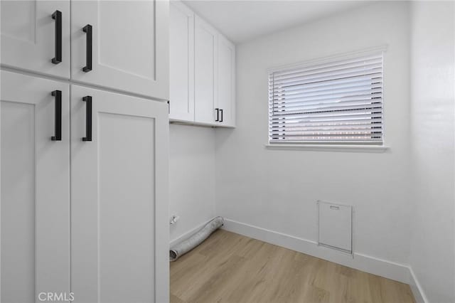 laundry area featuring cabinet space, baseboards, and light wood finished floors