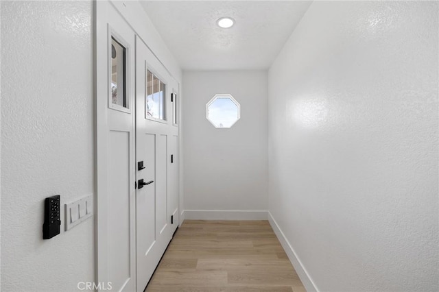 entryway with light wood-type flooring, baseboards, and a textured ceiling