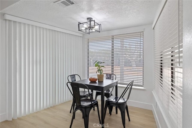 dining space featuring light wood-type flooring, visible vents, a textured ceiling, baseboards, and a chandelier