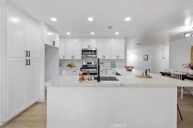 kitchen with light stone counters, appliances with stainless steel finishes, white cabinetry, and light wood-type flooring