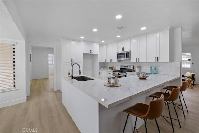 kitchen featuring light stone counters, light wood finished floors, stainless steel appliances, and a sink