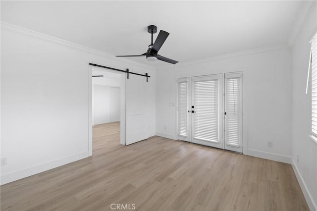 interior space with baseboards, light wood-style flooring, ceiling fan, ornamental molding, and a barn door