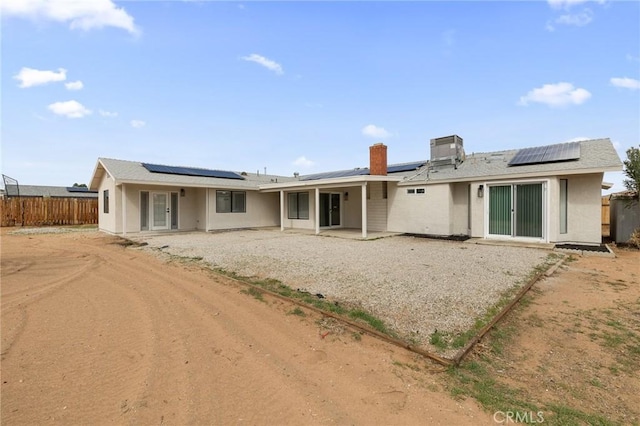 rear view of house featuring a patio area, fence, roof mounted solar panels, and stucco siding