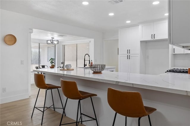 kitchen featuring a breakfast bar, light stone counters, recessed lighting, white cabinets, and light wood finished floors