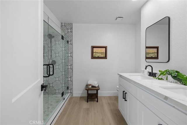 bathroom with visible vents, a shower stall, double vanity, wood finished floors, and a sink