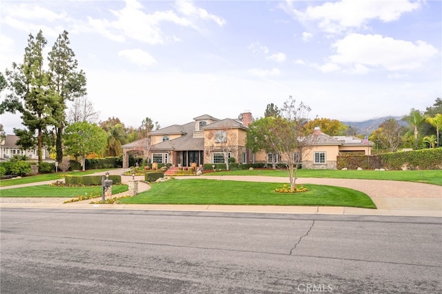 view of front facade with a front yard, a chimney, stone siding, and curved driveway